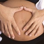 Postpartum physiotherapy client with hands forming a heart shape over her healing belly in Swords